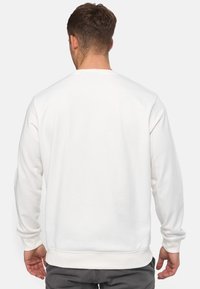 Sweat-shirt blanc avec un col ras du cou et des manches longues, avec une texture lisse et des poignets et un ourlet côtelés. Design simple et épuré sans logos visibles.