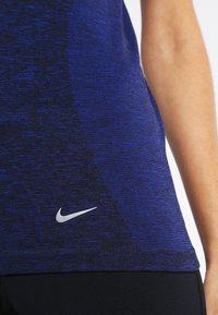 Modrá sportovní tílko s texturovaným designem, se stříbrným logem Nike na lemu a upnutým střihem.