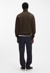 Rjava jopa z visokim ovratnikom, združena s črnimi cargo hlačami s sprednjimi žepi in gležnji prirezanim robom. Priložnostni športni copati.