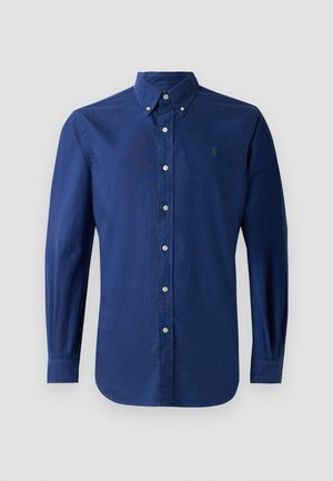 Chemise boutonnée bleu marine en tissu coton, avec un col pointu, des manches longues et un petit logo vert sur la poitrine gauche.