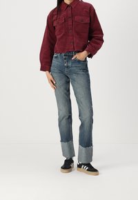 Bordeaux velour afsluttet skjorte med to brystlommer, parret med falmede blå straight-leg jeans med frynsede kanter og sorte sneakers.