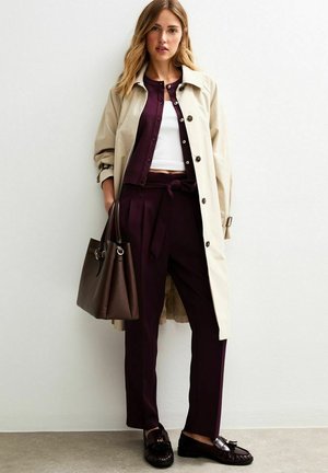 Beige trench coat over a burgundy cardigan and white top, with burgundy pants and black loafers. Includes a brown handbag.