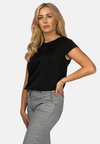 Czarna, krótka bluzka z okrągłym dekoltem, zestawiona z dopasowanymi spodniami w czarno-białą kratkę, ukazującymi gładką teksturę.