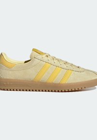 Baskets basses en daim beige avec trois rayures jaunes, lacets, col rembourré et semelle en caoutchouc classique.