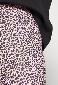 Różowe legginsy z czarno-limonkowym wzorem w panterkę; wykonane z elastycznego materiału, charakteryzujące się gładką teksturą i dopasowanym krojem.