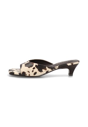 Mule de punta abierta con tacón bajo de estilo kitten, presenta un patrón de estampado de vaca en negro y beige en la parte superior y la suela.