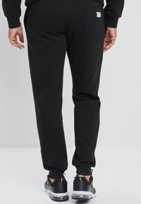 Zwarte sweatpants van katoen met een tapered fit, voorzien van een achterzak en geribde manchetten. Gecombineerd met zwarte sportschoenen.