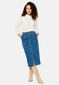 Modra jeans midi krila s sprednjimi gumbi, dvema stranskima žepoma in sprednjim razporkom. V kombinaciji z belim pletenim topom in bež škornji.