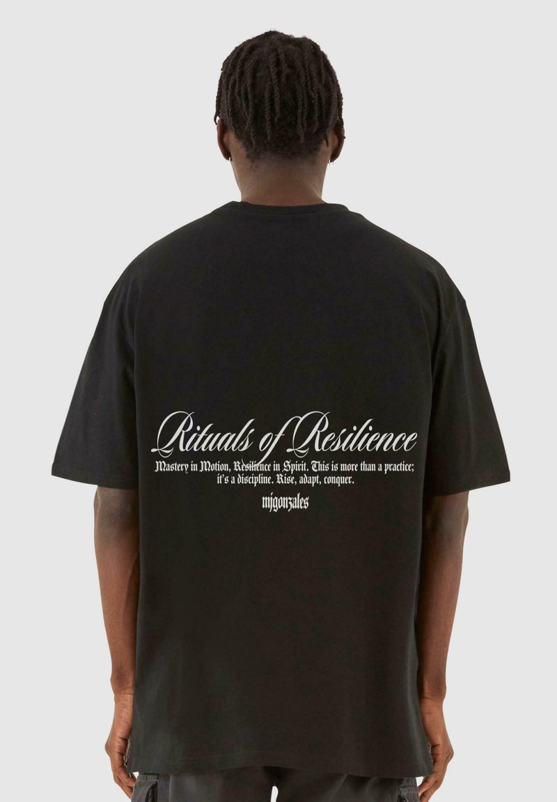 Tricou oversized negru, cu text alb pe spate, într-un font decorativ, detaliind fraze despre reziliență și stăpânire.