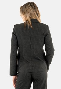 Blazer negro con rayas finas y corte entallado. Presenta un cuello de solapa y mangas largas, con un suave brillo en la textura de la tela.