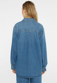 Denim shirt in light blue, featuring a collared neckline, long sleeves with buttoned cuffs, and a yoke seam detail on the back.