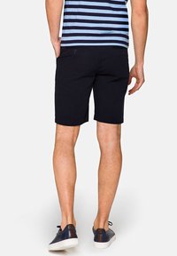 Granatowe szorty z mieszanki bawełny, długość do połowy uda, z dwiema tylnymi kieszeniami i gładką fakturą, w zestawieniu z granatowymi butami.