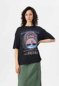 Black oversized t-shirt featuring a colorful graphic design with text, mountain, and celestial motifs. Short sleeves and relaxed fit.