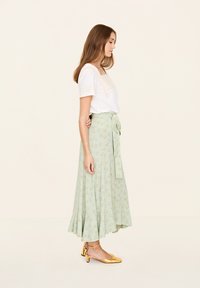 Weißes Baumwolloberteil mit besticktem Ausschnitt, kombiniert mit einem rock in Creme und mintgrün mit Blumenmuster und goldenen Blockabsatzschuhen.