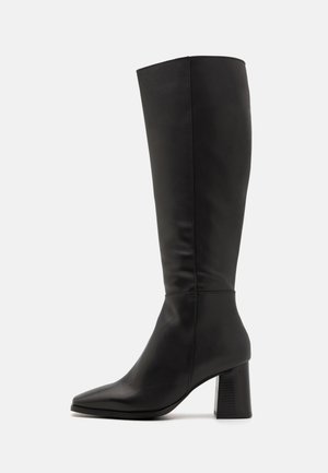 Fekete, térd fölé érő csizma sima bőrből. Hegyes orra és vastag, texturált tömbsarka van. Minimális varrási részletekkel.