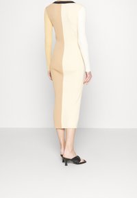 Abito midi a coste con maniche lunghe; presenta tre blocchi di colore: beige, crema e bianco, e un colletto nero. Texture liscia, aderente.