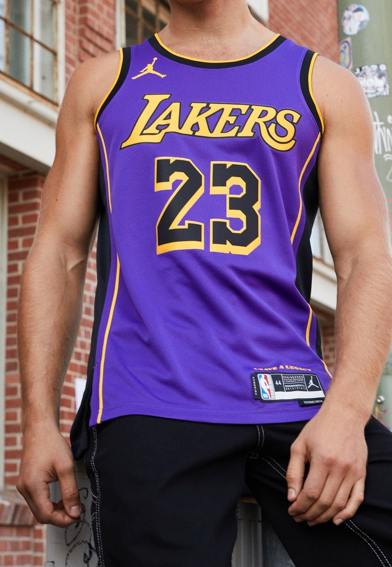 Lila baskettröja med gula detaljer, pryds av "LAKERS" och nummer "23", tillverkad av ventilerande tyg, kompletterad med svarta sidopaneler.