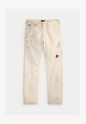 Kremo spalvos kelnės su daugybe mažų išblukusių ir raudonų spausdintų logotipų, tekstų ir simbolių, išsibarsčiusių ant priekinių kojų ir kišenių.