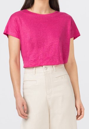 Haut fuchsia à manches courtes avec un col large, présentant une texture chinée subtile. Associé à un pantalon taille haute couleur crème.