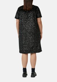 Czarna sukienka z cekinami z krótkimi rękawami, sięgająca do kolan, z okrągłym dekoltem i gładkiej tkaniny; noszona z czarnymi butami i ciemnymi skarpetkami.