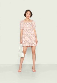 Vestido mini com padrão floral em rosa e branco, apresentando mangas bufantes, um decote quadrado e um ajuste solto. Acentuado com saltos claros em rosa e uma bolsa branca.