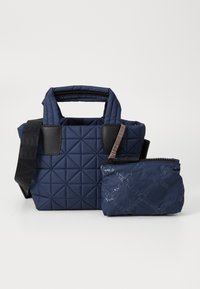 Granatowa torba tote pikowana z czarnymi skórzanymi akcentami i górnymi uchwytami; zawiera mniejszą dopasowaną saszetkę z detalem logo i zapięciem na zamek.