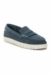 Mocasines de ante en azul oscuro con una suela de goma blanca. Presenta una costura decorativa y un acento elevado en el talón. Diseño clásico de calzado tipo slip-on.