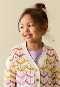 Gebreid vest in crèmekleur met multicolor golvende patronen in oranje, geel, roze en paars. Voorzien van een V-hals en twee knopen.