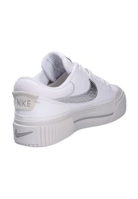 Witte sportieve schoen met een gestructureerde zilveren Swoosh, gevoerde kraag en een dikke, gegroefde witte zool. Inclusief "NIKE" branding op de hiel.