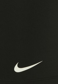 Černý sportovní top s žebrovanou texturou a bílým logem Nike na spodní levé straně. Navržený pro pohodlí a flexibilitu.