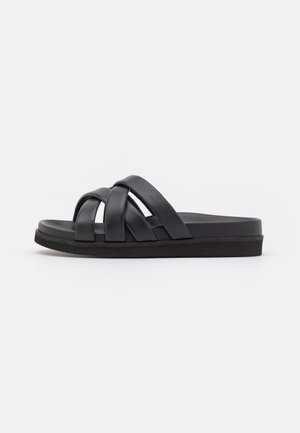 Las chanclas negras cuentan con tres correas superpuestas, un diseño plano y una suela texturizada. El material parece suave con un sutil brillo.