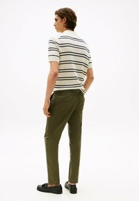 Polo a righe crema con strisce navy, abbinato a pantaloni verdi oliva a sigaretta. Mocassini neri completano il look. Design semplice e casual.