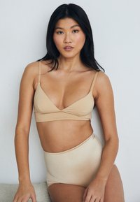 Beige bra and high-waisted briefs made of smooth fabric. Bra has a V-neck design with thin straps; briefs feature a seamless waistband.