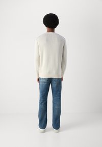 Suéter de punto crema con bajo acanalado, combinado con jeans azul de pierna recta. Los jeans tienen una textura desgastada y un ligero desgarro.