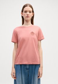 Rosa bomull t-skjorte med korte ermer, med en teksturert logo på brystet. Kombinert med vide, lyseblå denim bukser.
