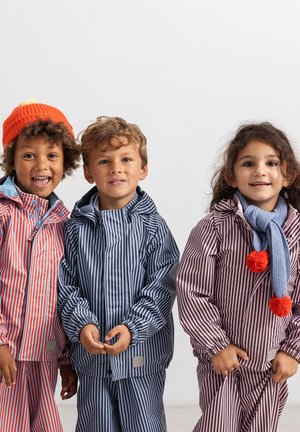 Trois enfants portant des imperméables rayés, l’un avec un chapeau orange, un autre avec une écharpe bleue, debout côte à côte sur un fond uni.