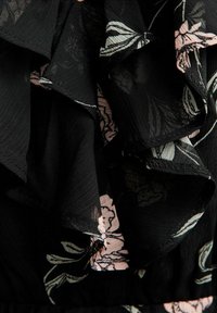 Zwarte stof met gelaagde ruches, voorzien van een roze en wit bloemenpatroon en zichtbare naadstiksels.