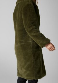 Olivengrøn pelsfrakke i imiteret pels med lange ærmer, en krave og sidelommer. Blød tekstur og lige snit, der går til midt på låret.