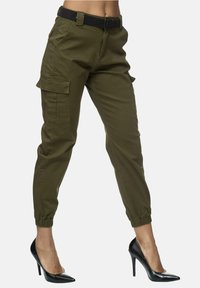 Pantalons cargo vert olive avec des poignets élastiques et deux poches latérales, associés à des chaussures à talons hauts noires. Comprend une ceinture noire à la taille.