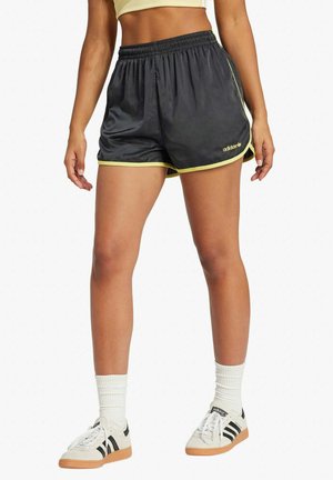 Pantalones cortos deportivos negros con un diseño transpirable, cintura elástica y acentos en amarillo neón. Combinados con calcetas blancas y zapatillas de color crema.