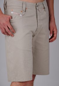Beige shorts made of cotton with a straight cut, featuring a coin pocket, copper-tone hardware, and visible stitching details.