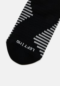 Chaussette noire avec un motif texturé de rayures horizontales blanches, comportant "Gauche 10" imprimé en blanc sur la pointe.