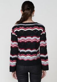 Pull en maille noire avec un motif en zigzag rose, gris et blanc. Manches longues, encolure ras du cou et détails en points ouverts tout au long.