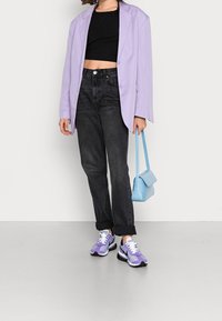 Blazer large couleur lavande, crop top noir, jean taille haute foncé, mini sac à main bleu clair, et baskets violettes avec accents blancs.