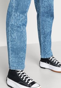 Světle modré džíny z denimu s texturovaným vzorem po celé ploše, doplněné černými vysokými teniskami s bílými akcenty a robustní podešví.