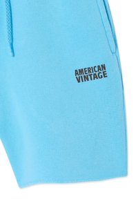 Section de tissu bleu clair d'un vêtement avec un cordon de serrage et le texte noir "AMERICAN VINTAGE" imprimé à sa surface.