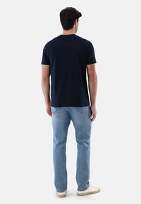 Marineblaue Baumwoll-T-Shirt mit Rundhalsausschnitt, kurzen Ärmeln und figurbetontem Schnitt, kombiniert mit hellblauen Jeans und weißen Schuhen.