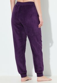 Violetti fleece-housut, joissa on joustava vyötärö ja ribbi-taskut, jotka houkuttelevat sileällä pinnalla, kapealla muodolla ja ilman näkyviä taskuja.