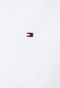 Tessuto di cotone bianco con logo ricamato a forma rettangolare nei colori nero, bianco e rosso al centro.