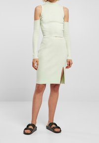 Hellgrünes geripptes zwei-teiliges Outfit bestehend aus einem cropped High-Neck-Top mit kaltem Schulterdesign und einem knielangen Rock mit seitlichem Schlitz.